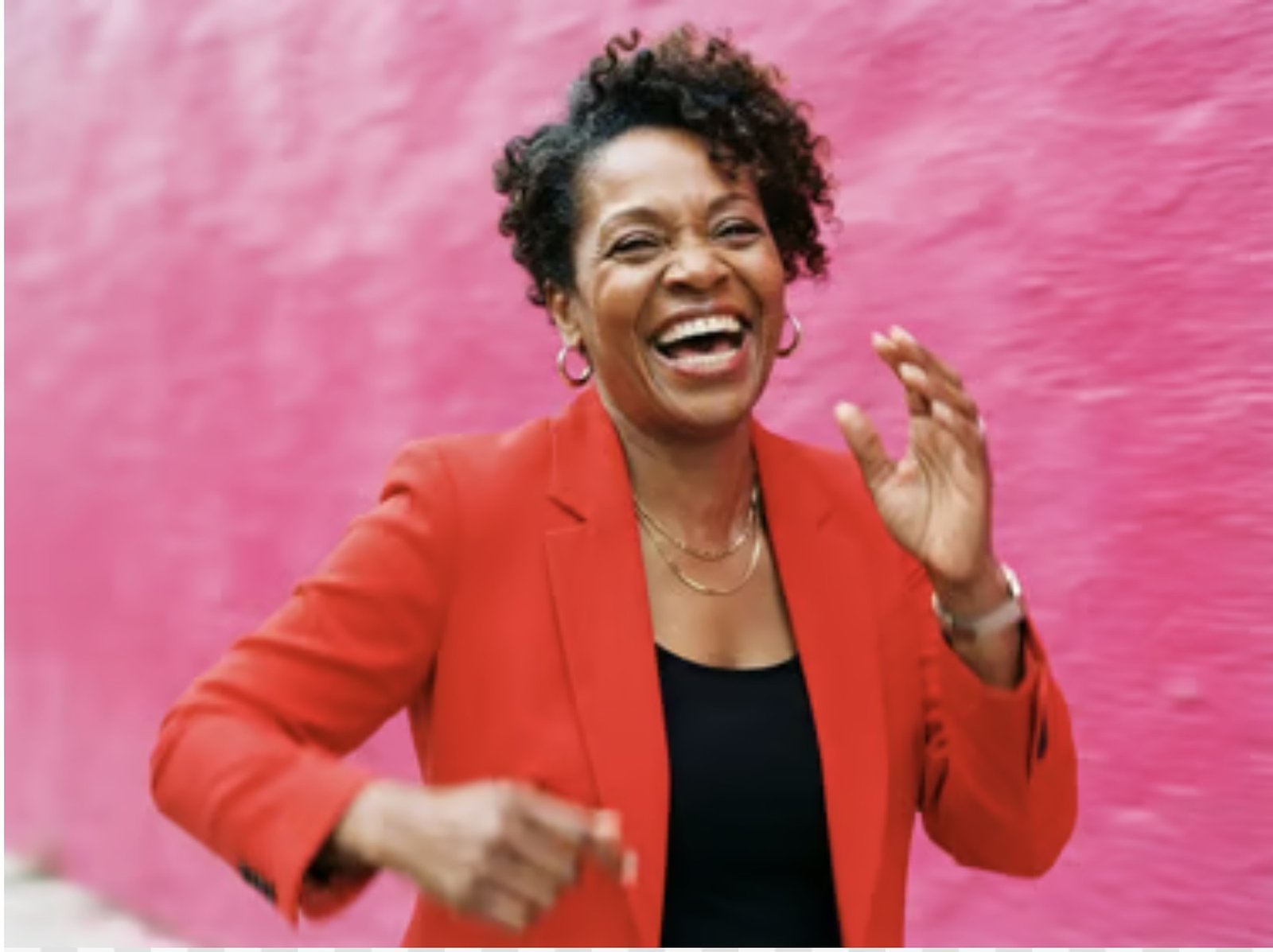 A woman laughing, delighted, against a wall of hot pink