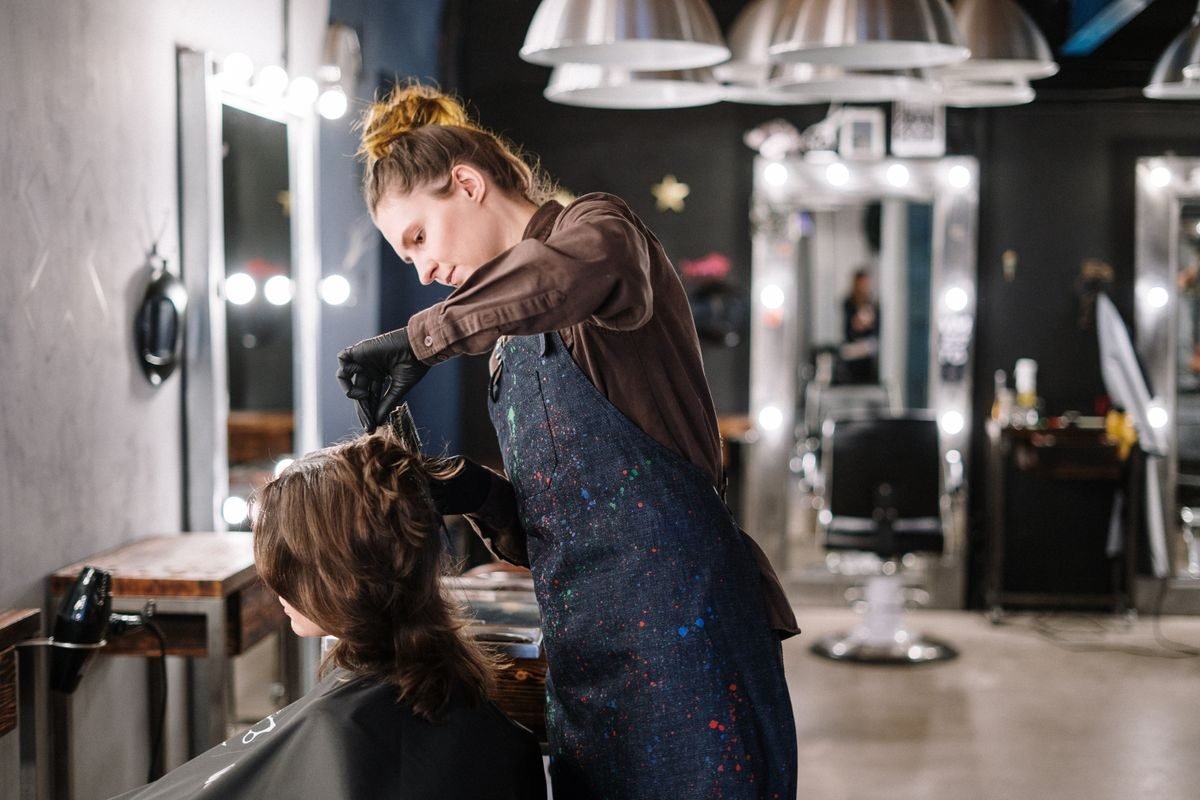 A hairdresser at work in a bright salon, styling her client&rsquo;s hair